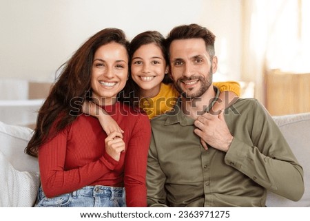 Family Portrait. Cheerful arab father, mother and daughter posing embracing at home, kid girl hugs her young parents smiling to camera, sitting on sofa in living room indoor. Bonding time concept