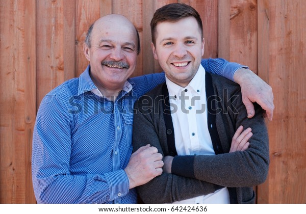 Family portrait. Father-in-law embraces\
the son-in-law. They are smiling at the\
camera.