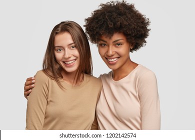 Family portrait of happy mixed race sisters hug each other, have satisfied expessions, smile pleasantly, being in high spirit, wear casual jackets isolated on white background. Interracial friendship