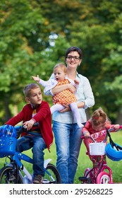 Family Portrait Outdoor In Park. Modern Mom With Kids. Child Learning To Ride Bike