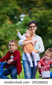 Family Portrait Outdoor In Park. Modern Mom With Kids. Child Learning To Ride Bike