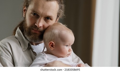 Family Portrait Serious Caucasian Bearded Dad Father Man Holding Hugging Small Infant Newborn Girl Boy Kid Daughter Son Kiss At Head Looking At Camera At Home. Closeup Daddy Kissing Adopted Child