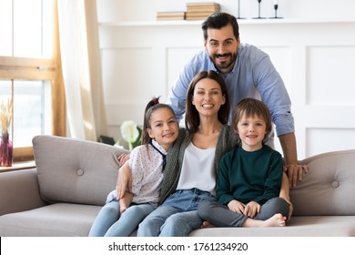 Family portrait smiling parents with children sitting on cozy couch, posing for photo, looking at camera, happy father standing behind beautiful young mother hugging daughter and son, sitting on sofa - Shutterstock ID 1761234920