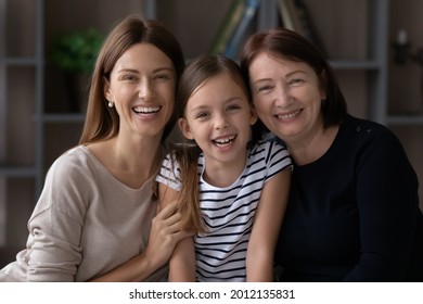 Family Portrait Of Three Female Generations. Millennial Mom, Older Grandma An Preteen Daughter Kid Hugging Together, Looking At Camera, Smiling, Laughing. Intergenerational Headshot