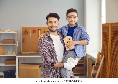 Family Portrait Of Young Father With His Favorite Little Son In Home Workshop Or Garage. Skillful Master Carpenter Holds A Boy In Goggles. Dad Teaches His Son Handicraft Skills In A Carpentry Shop.