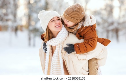 Family portrait of young happy mother holding cute little boy son on back while walking together in snowy winter park. Active young mom giving piggyback ride to small kid outdoors on cold frosty day - Powered by Shutterstock