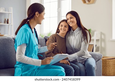 Family practitioner or pediatrician doing a home visit. Happy young woman doctor in scrubs and smiling mother and child daughter sitting on the sofa in the living room and talking - Powered by Shutterstock