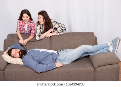 Family Prank. Mom And Daughter Going To Cut Beard Sleeping Dad. Lets Have Fun. Cheerful Girls With Scissors Cut Long Fathers Beard. Just For Fun. He Needs Beard Grooming. Cut His Beard. Girlish Team.