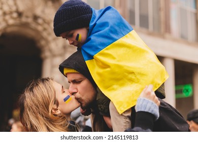 Family pray to stop war. Woman kiss her man, child sitting on man's shoulders. Child and mother with blue and yellow Ukrainian flag on they cheek, woman wrapped in Ukrainian flag. Support Ukraine.