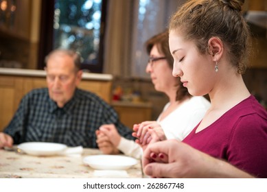 Family Praying At Dinner Time. Foreground In Focus, Blurred Background, Natural Light