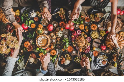 Family praying holding hands at Thanksgiving table. Flat-lay of feasting peoples hands over Friendsgiving table with Autumn food, candles, roasted turkey and pumpkin pie over wooden table, top view - Shutterstock ID 1543085186