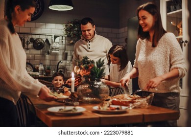 Family preparing traditional festive Christmas Eve dinner together in cozy homely atmosphere, two daughters helping parents to set New Years table, cooking in kitchen decorated for winter holidays
