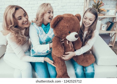 Family Presenting Toy Bear to Smiling Daughter. Gift on Birthday. Mother with Daughter. Smiling Women. Sitting on Sofa. Celebration Concept. Happy Family. Sitting at Home. Holiday in March.