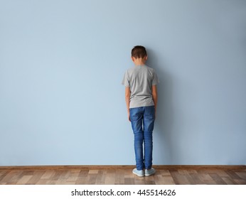 Family problems concept. Punished boy standing near wall