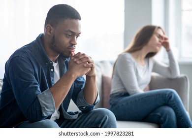 Family Problems. Portrait Of Upset Interracial Couple Sitting On Couch After Quarrel, Depressed Young Multicultural Spouses Suffering Relationship Crisis, Selective Focus On Sad Black Man - Shutterstock ID 1997823281