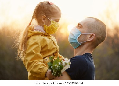 Family protection. A young father hugs his little girl daughter in the spring garden outdoors. Protective masks on faces from coronavirus infection