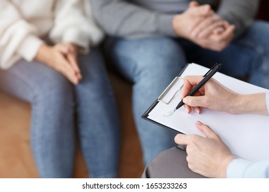 Family Psychologist. Professional Marriage Consultant Taking Notes Talking With Couple Sitting In Office. Selective Focus, Cropped
