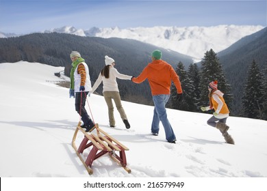 Family Pulling Sled Up Mountain Top Ski Slope