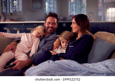 Family In Pyjamas Sitting On Sofa Watching TV Together As Children Fall Asleep