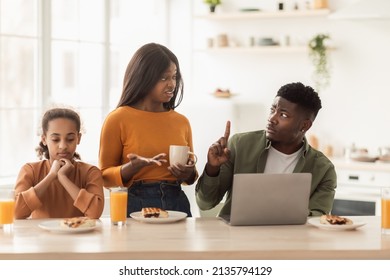 Family Quarrels. Discontented African American Parents Arguing Near Unhappy Little Daughter Having Lunch And Using Laptop Computer Sitting At Table In Modern Kitchen At Home. Relationship Problem