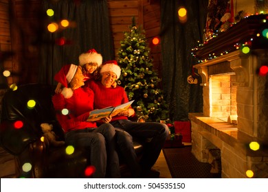 Family read Christmas book sitting on coach in front of fireplace in festive decorated interior - Powered by Shutterstock