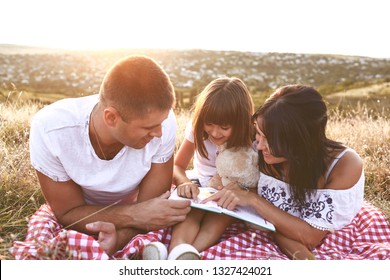 Family Is Reading A Book  In Nature.