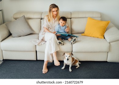 Family reading a book. Woman her son and small dog in living room reading book sitting on a beige sofa in sunny living room. early development of child. reading fairy tales and children's literature