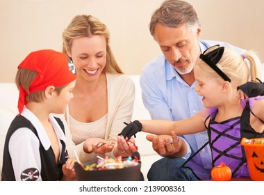 Family Ready To Feast. A Family Sitting Together And Sharing Sweets On Halloween With Children In Fancy Dress.