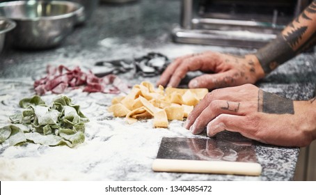 Family Recipe. Close-up Photo Of Male Chef's Hands With Tattoos Finishing Making Italian Pasta On The Kitchen Table With Flour