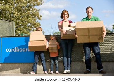 Family At Recycling Center Carrying Cardboard Boxes Smiling At Camera