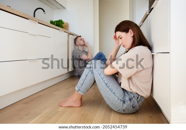 family, relationship\
and quarrel concept - portrait of divided couple sitting on the\
floor in the kitchen