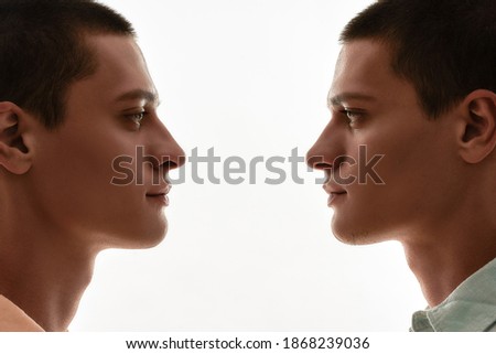 Family relationships concept. Silhouetted portrait of two young caucasian twin brothers looking at each other while standing face to face isolated over white background
