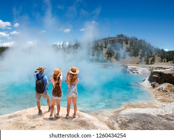 Family Relaxing And Enjoying Beautiful View Of Gazer On Vacation Hiking Trip. Friends On Hiking Trip. Excelsior Geyser From The Midway Basin In Yellowstone National Park. Wyoming, USA