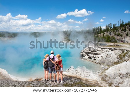 Family relaxing and enjoying beautiful view of gazer on vacation hiking trip. Father with arms around his family. Excelsior Geyser from the Midway Basin in Yellowstone National Park. Wyoming, USA