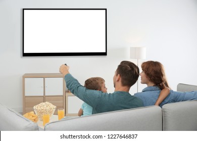 Family with remote control sitting on couch and watching TV at home, space for design on screen. Leisure and entertainment - Shutterstock ID 1227646837