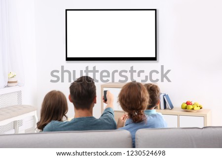 Family with remote control sitting on couch and watching TV at home, space for design on screen. Leisure and entertainment