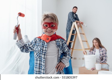 Family Renovating Their Home And Painting Walls, The Boy Is Wearing A Superhero Costume And Holding A Paint Roller