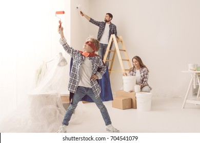 Family Renovating Their Home And Painting Walls, The Boy Is Wearing A Superhero Costume And Holding A Paint Roller