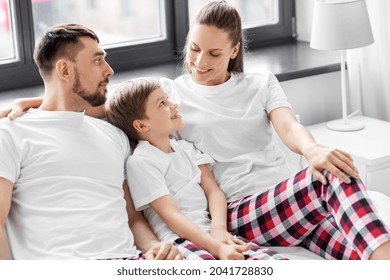 Family, Rest And People Concept - Happy Mother, Father And Little Son In Matching Pajamas Sitting In Bed In Morning