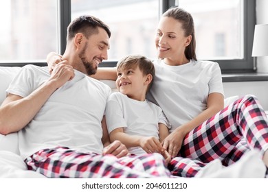 Family, Rest And People Concept - Happy Mother, Father And Little Son In Matching Pajamas Sitting In Bed In Morning