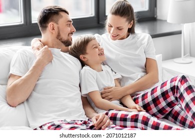 Family, Rest And People Concept - Happy Mother, Father And Little Son In Matching Pajamas Sitting In Bed In Morning