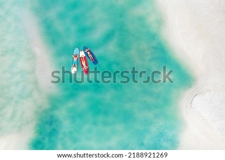 The family is resting lying on Sup boards in the turquoise sea. Three people ride sup boards in the ocean near the beach 