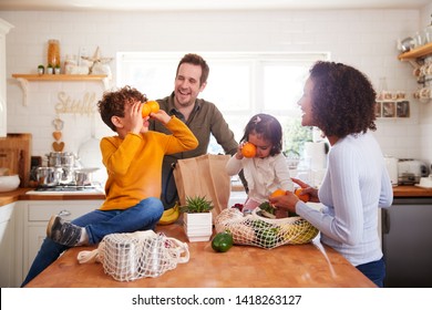 Family Returning Home From Shopping Trip Using Plastic Free Bags Unpacking Groceries In Kitchen