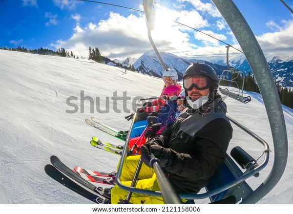 Family riding ski lift cable car on winter\
vacation skiing. Family on winter vacations ski trip taking\
selfie on ski lift with amazing mountain view of the ski resort and\
slopes. Active family