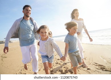 Family Running On Sandy Beach At Sunset