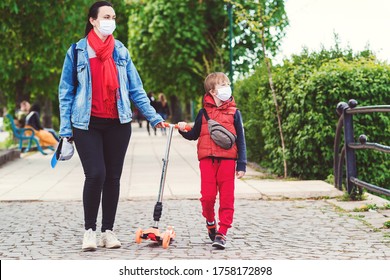 Family In Safety Masks Outdoors. Riding Boy On Scooter In Park. Boy Wears Medical Face Mask. Real Life 2020. Coronavirus Epidemic. Mother And Son On A Walk During Coornavirus Quarantine.