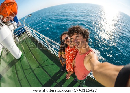 The family is sailing on a cruise ship, a girl with husband and son are standing at the fence on the ship and looking at the sea, traveling by ferry, a boy with mom and dad take selfies on the ocean.