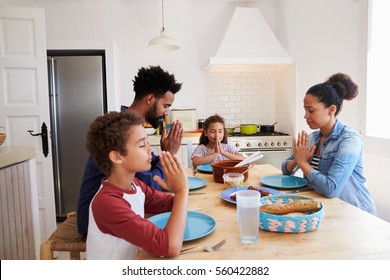 Family saying grace at the kitchen table before their meal