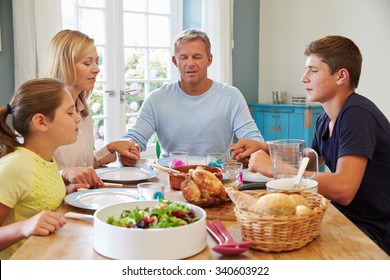 Family Saying Prayer Before Enjoying Meal At Home Together