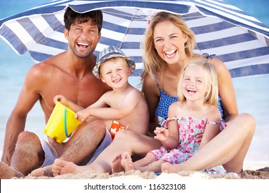 Family Sheltering From Sun Under Beach Umbrella